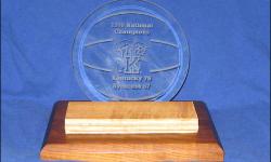 Display that features an actual piece of the floor used during the 1996 NCAA Final Four. Kentucky defeated Syracuse to win the Championship. Mounted on a wood base, along with a re-moveable round beveled etched glass that shows the final score and